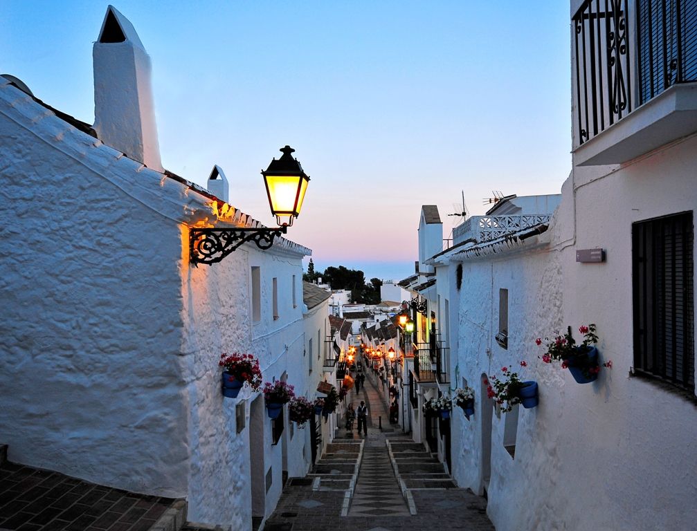 Calle empedrada de Mijas pueblo blanco al atardecer con macetas de flores