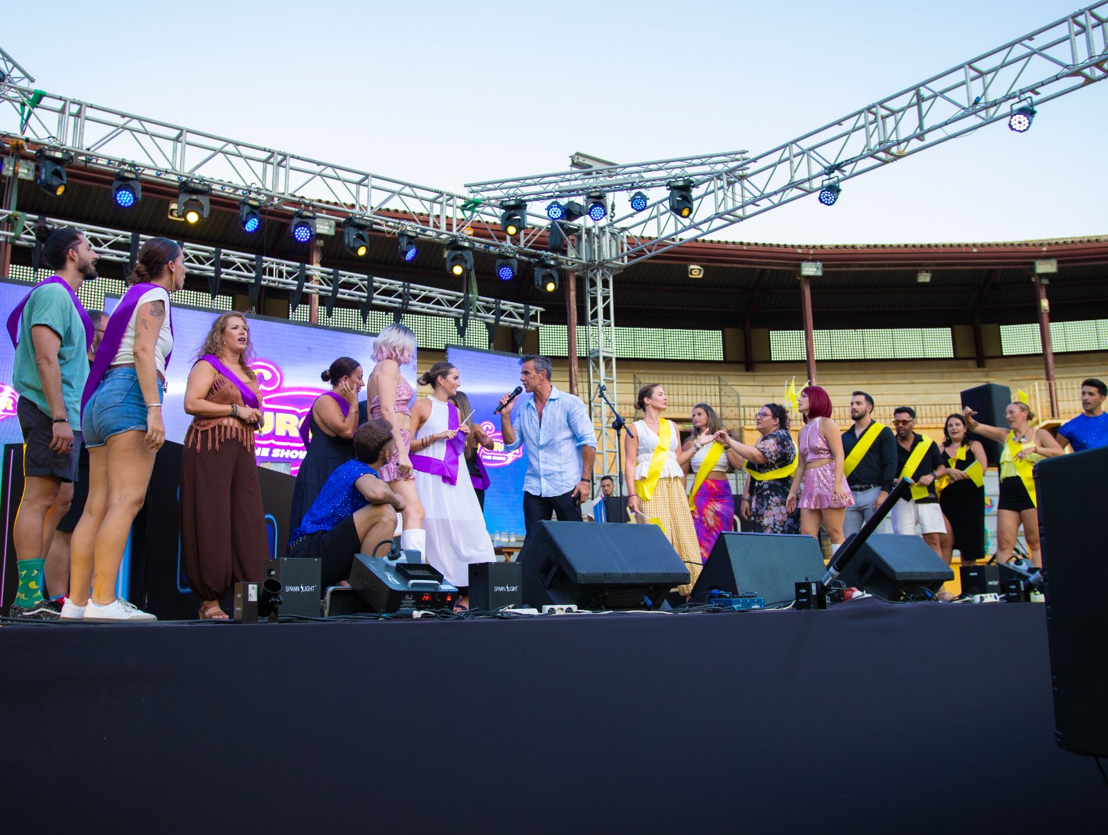 Concursantes del equipo morado y del equipo amarillo sobre el escenario con Alonso Caparrós y su micrófono en Furor The Show