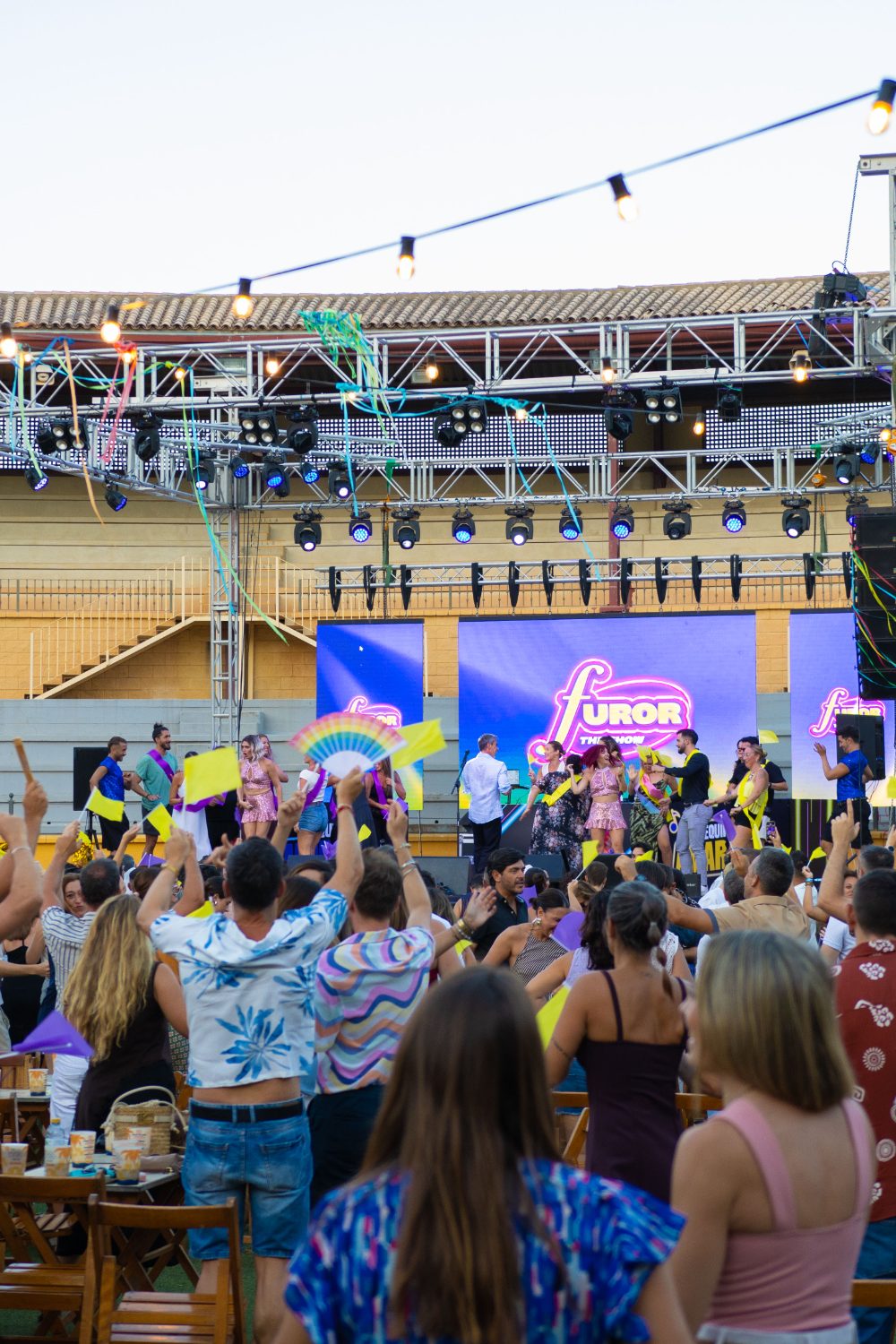 Público del equipo amarillo animando con banderines frente a la pantalla de Furor The Show en Plaza Paraíso Torremolinos