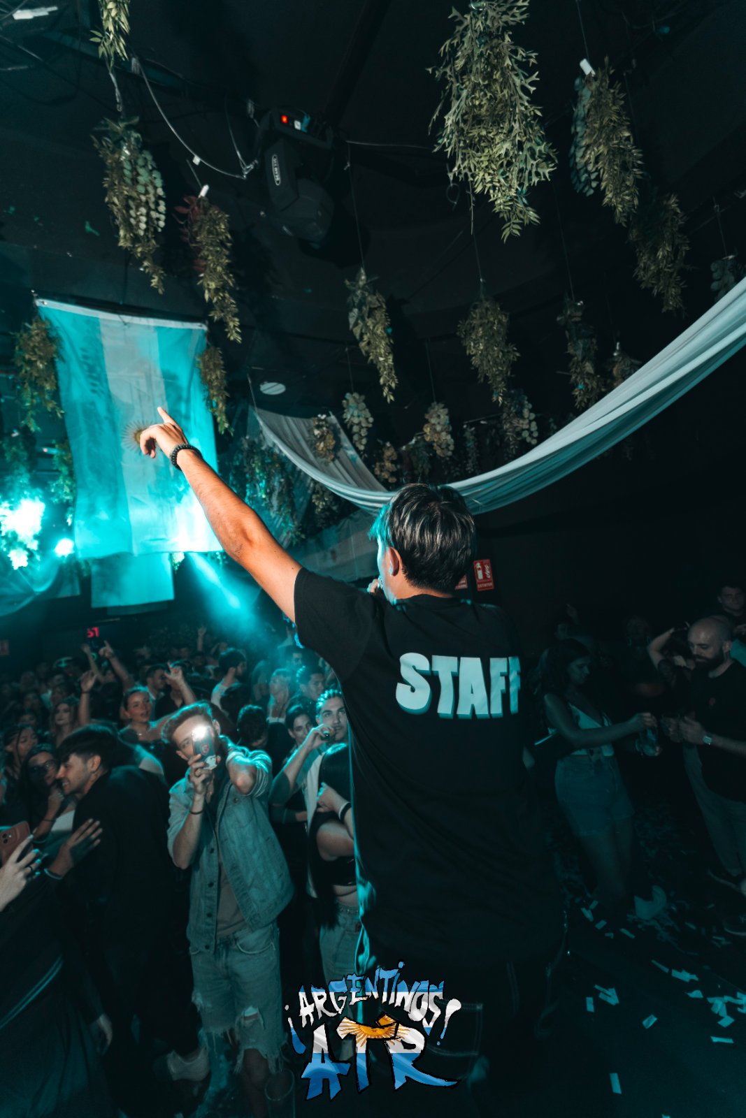 Miembro del staff de Argentinos ATR señalando la bandera de Argentina colgada sobre la pista mientras el público graba con el móvil