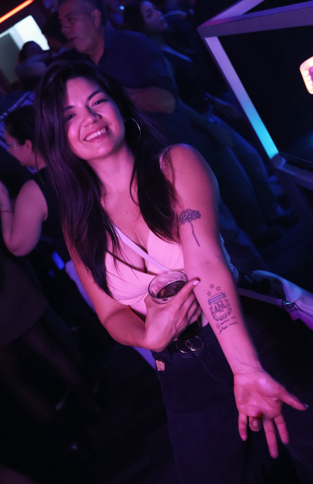 Chica sonriendo y mostrando su tatuaje del escudo de la AFA con una copa en la mano durante el tardeo argentino