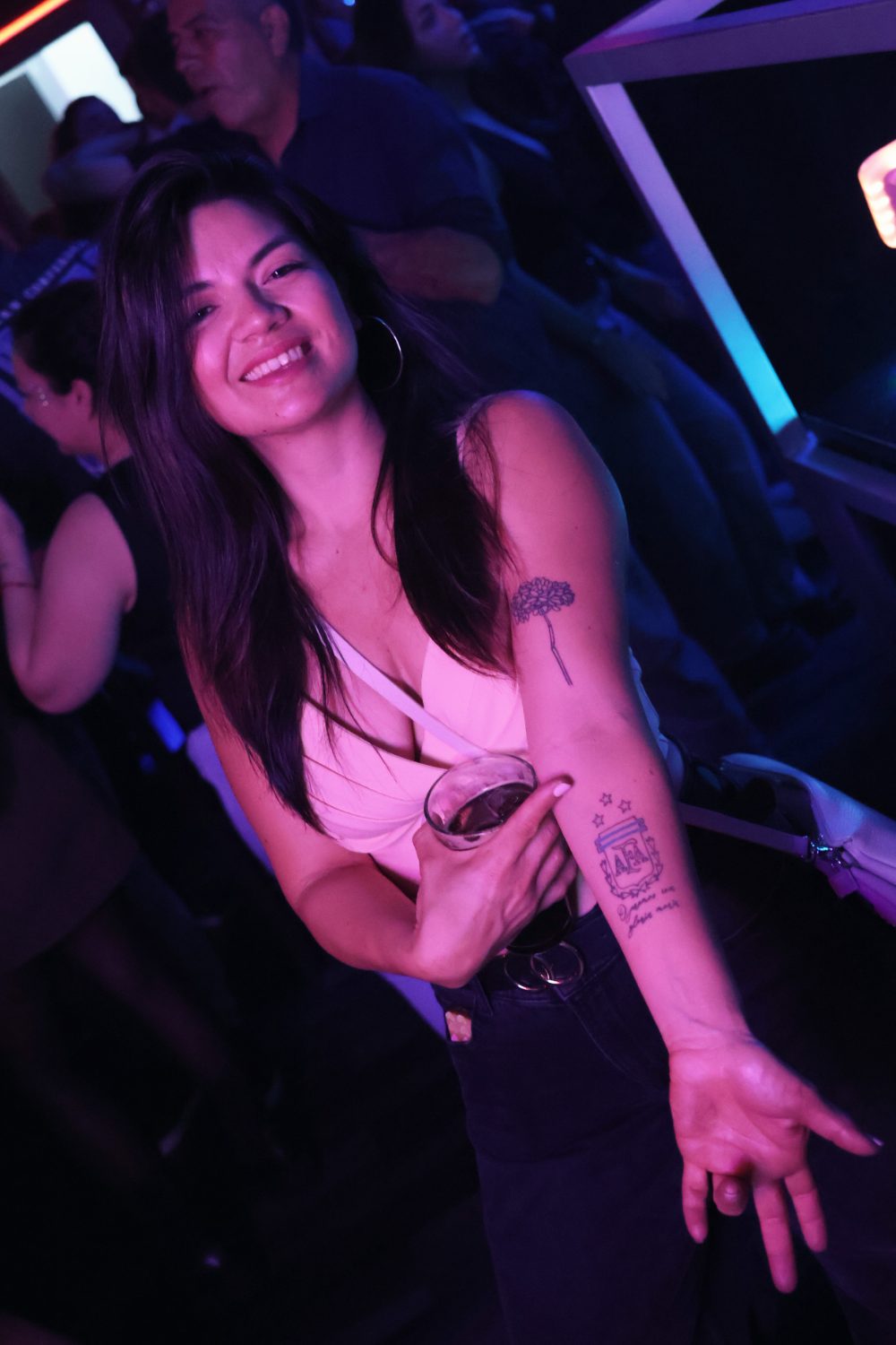 Chica sonriendo y mostrando su tatuaje del escudo de la AFA con una copa en la mano durante el tardeo argentino