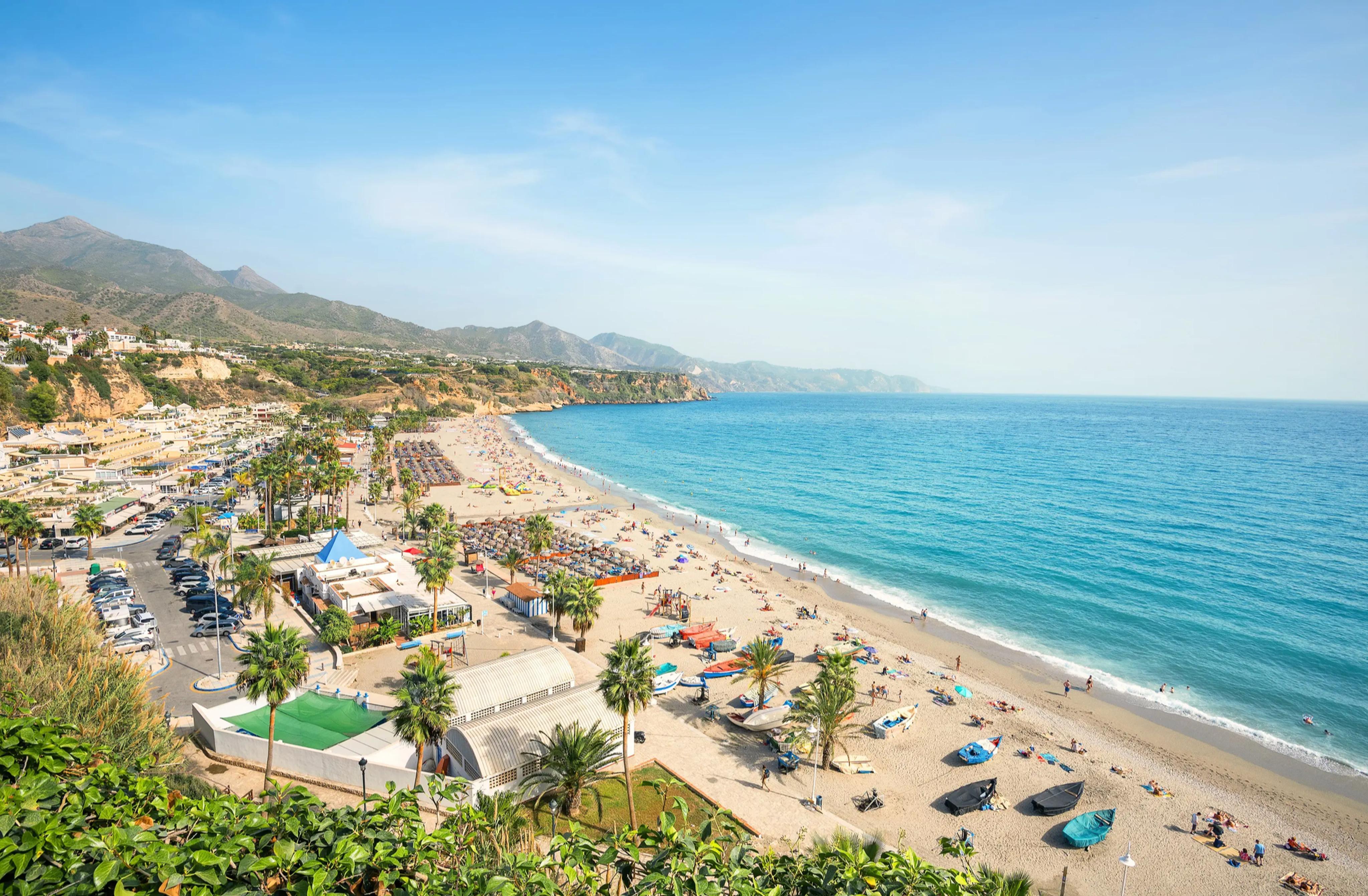 Vista aérea de la Costa del Sol en verano: playa llena de sombrillas, palmeras y el mar Mediterráneo azul turquesa en Torremolinos, Málaga